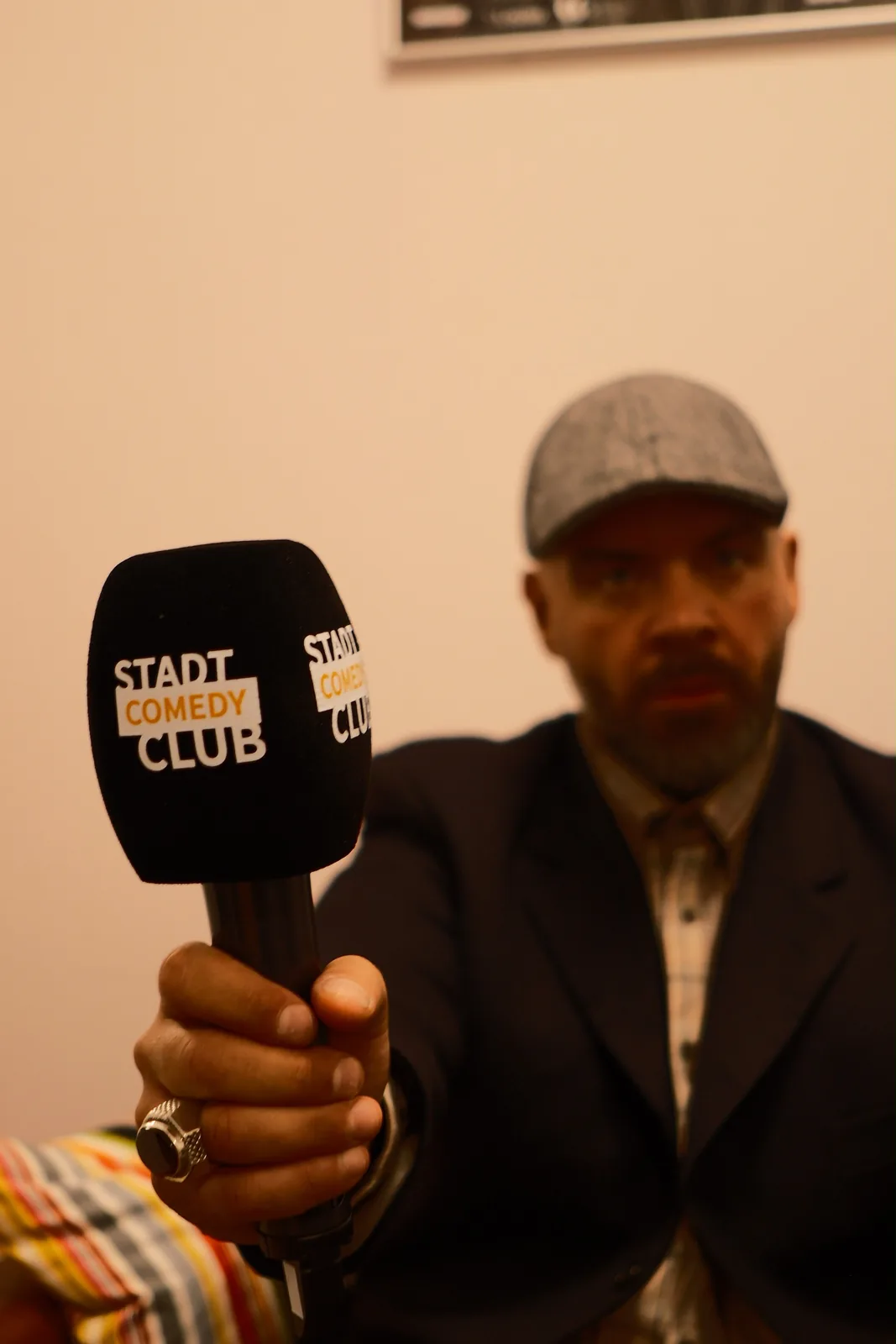 Ein Mikrofon mit dem Logo des StadtComedyClub, dahinter ein Comedian.